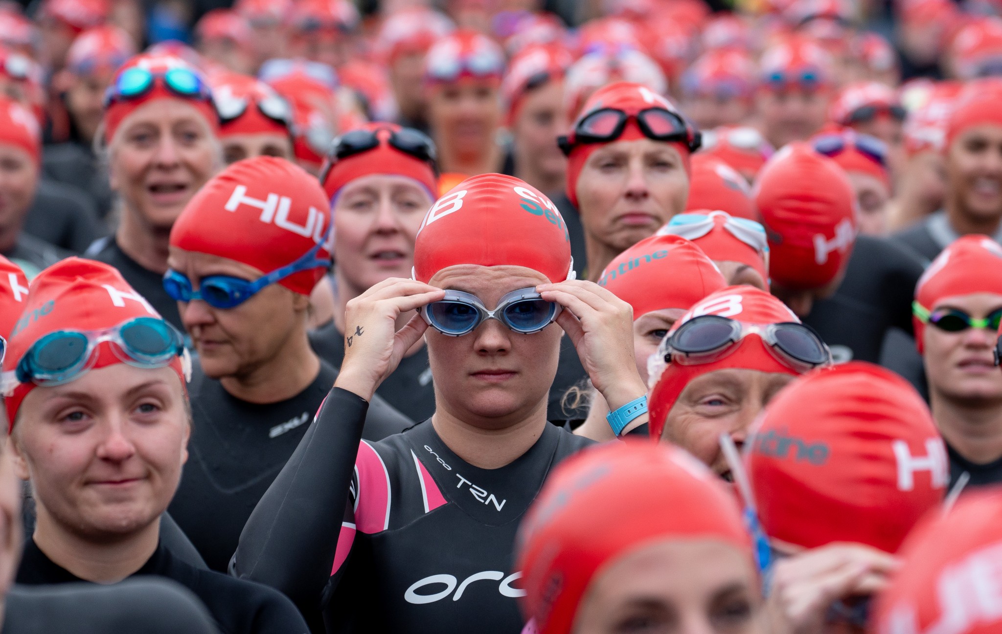 people standing getting ready to swim in the serpentine with red caps