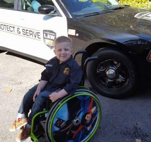 Medulloblastoma survival stories: Blake in a wheelchair next to a police car