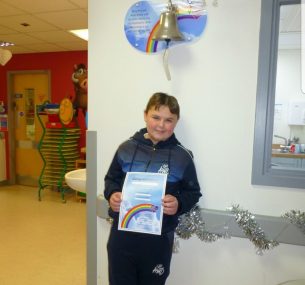 boy holding certificate standing underneath end of treatment bell