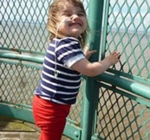 Lucy smiles, holding onto a metal fence.