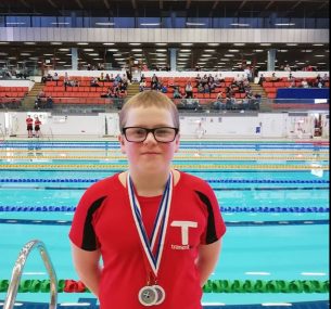 Boy in red top with medals in front of swimming pool