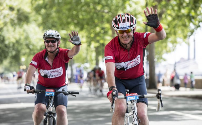 Two cyclists waving at the camera at the Prudential ride London 100