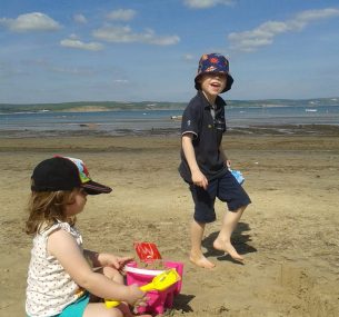 Owen standing with black shorts and shirt by the beach