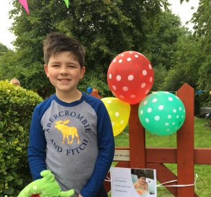 Boy standing next to gate with balloons