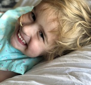 girl with blue top and blond hair lying in bed with feeding tube