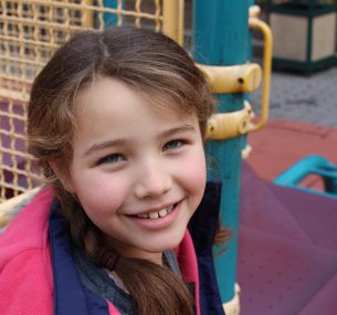 Girl smiling to camera with plaits and pink hood