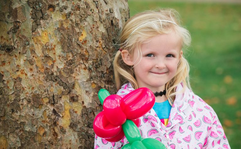 Daisy holding balloons, leaning against a tree