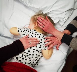 Girl in hospital bed with parents hand on back