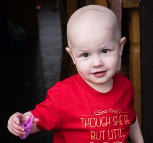 Bald girl with red top holding purple clothes peg