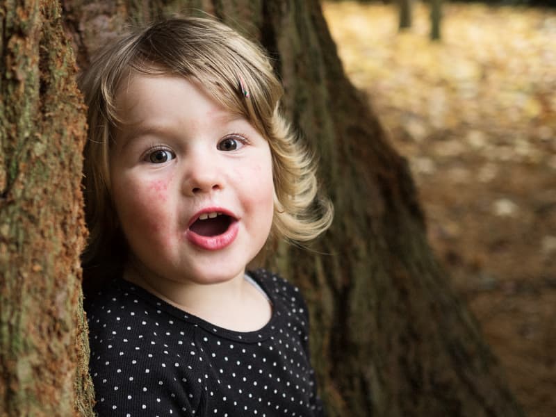 Girl with short hair and polka dot top standing against a tree