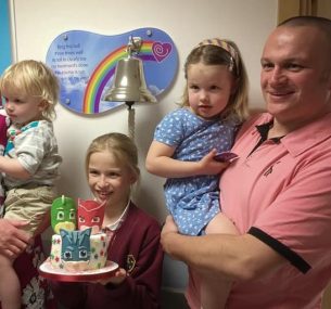 Family in front of bell holding a cake