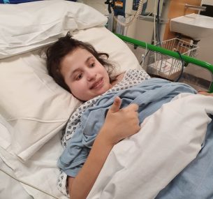 Girl in hospital bed with thumbs up