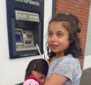 Blind girl in grey top standing outside cash point