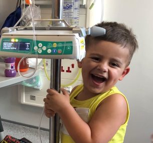 Smiling boy in yellow top holding machine in hospital