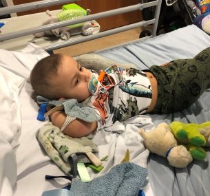 Boy in hospital bed with dummy and dinosaur t-shirt