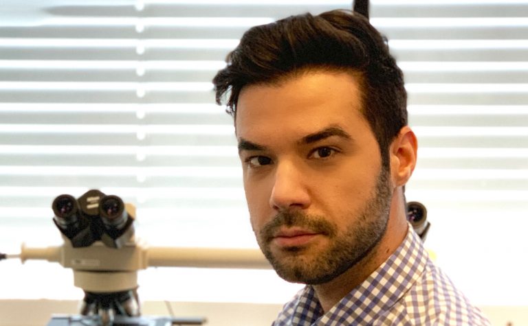 Researcher in lab with microscope looking at camera Srdan Rogosic