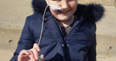 Girl with feeding tube in coat holding pebble