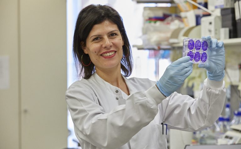 Female researcher smiling at camera holding a plate of cells