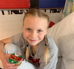 Blonde girl with plaits sitting in hospital bed with apple juice