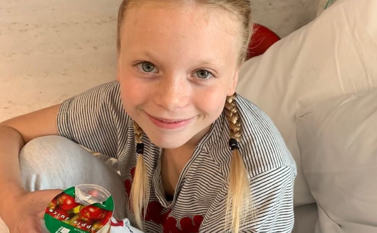 Blonde girl with plaits sitting in hospital bed with apple juice