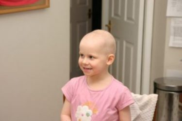 Esme girl with no hair with pink shirt smiling