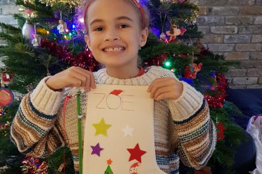 zoe girl smiling standing by a christmas tree holding a stocking
