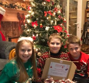 jacob and siblings by a christmas tree holding gift box