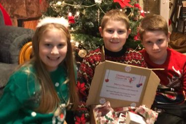 jacob and siblings by a christmas tree holding gift box