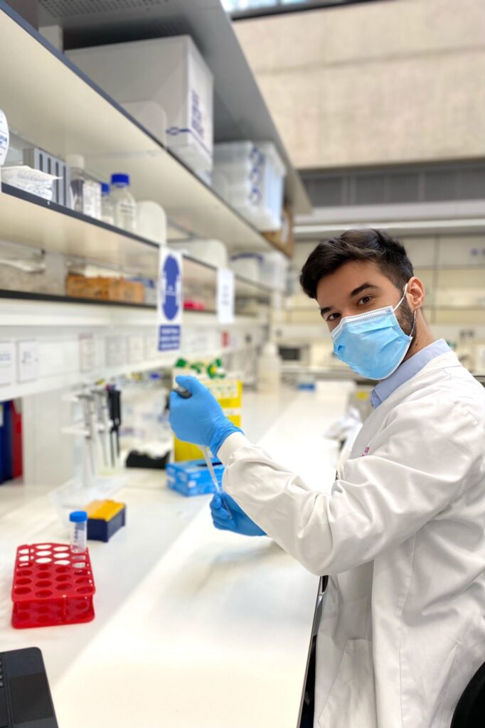 Researcher wearing mask and white lab coat holding pipette