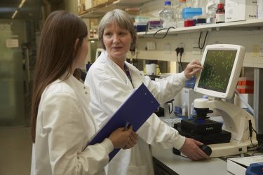 two researchers talking by a screen wearing white lab coats