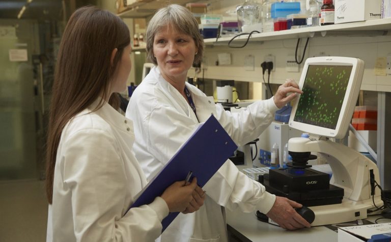 two researchers talking by a screen wearing white lab coats