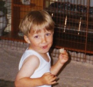Christopher as a toddler looking at camera eating and drinking bottled milk