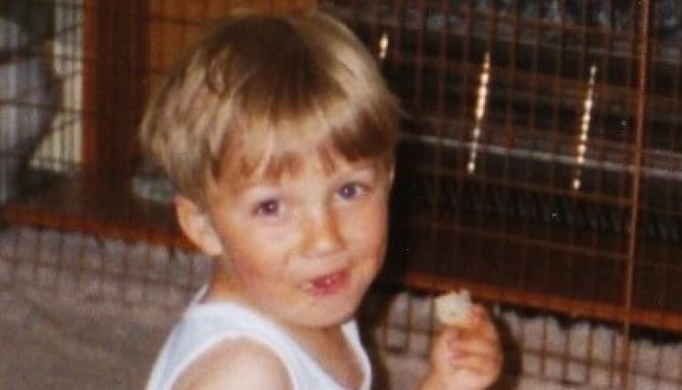 Christopher as a toddler looking at camera eating and drinking bottled milk