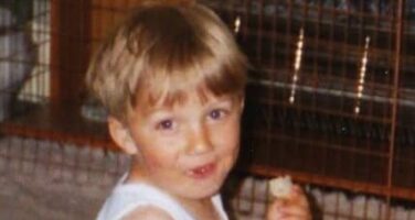 Christopher as a toddler looking at camera eating and drinking bottled milk
