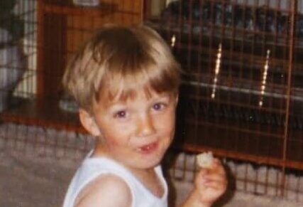 Christopher as a toddler looking at camera eating and drinking bottled milk