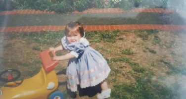 Lauren as a toddler hold a tric