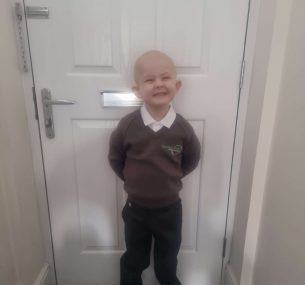 Finley standing by the door wearing school uniform with no hair