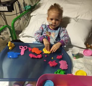 Young Bella Rose in her hospital bed playing with plasticene