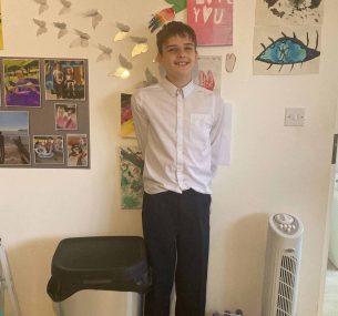 Kodie with school uniform standing smiling by the wall min x2