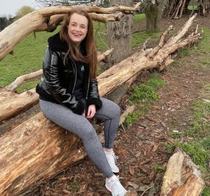 Ellen sitting on a fallen tree smiling at camera min