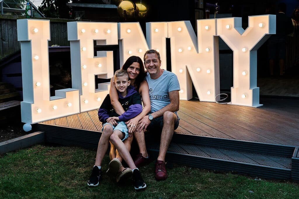 Lenny and his parents sitting witha big Lenny LED sign BEHIND THEM