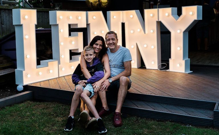 Lenny and his parents sitting witha big Lenny LED sign BEHIND THEM