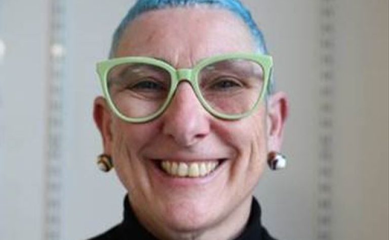 Professor Faith Gibson with green glasses and blue hair..