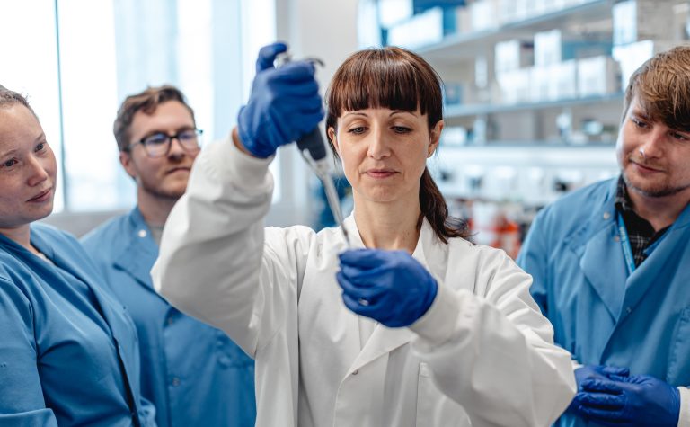 3 researchers watching female researchers with pipette min