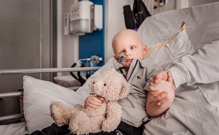 Jack sitting in hospital bed holding his mums hand