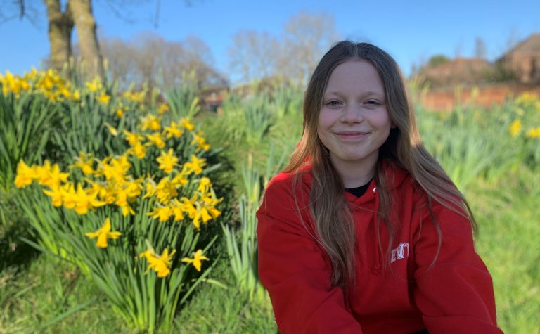 Eve smiling at camera sitting next to daffodils in red hoodie