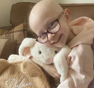Dulcie smiling at the camera, cuddling a bunny rabbit teddy