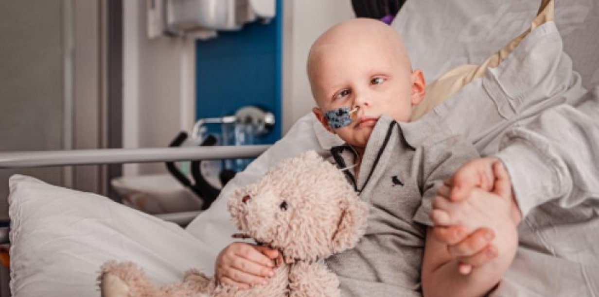 a boy with cancer receiveing treatment at the hospital. His mother holds his hand.