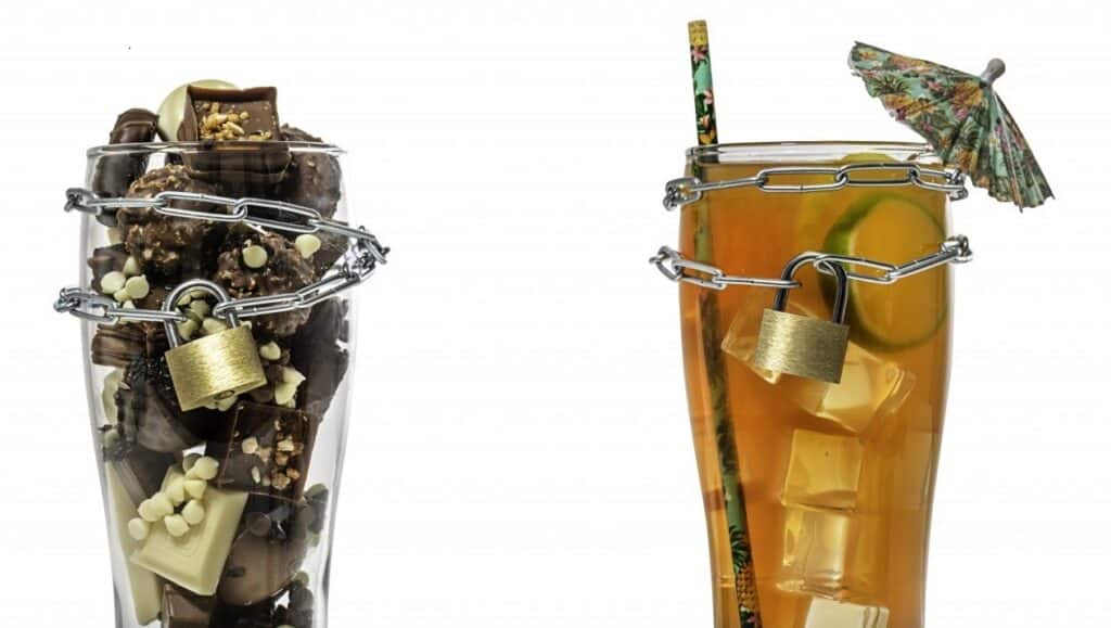 Two glasses filled with sweets and iced tea locked with chains and padlocks, symbolizing restricted access to sugary treats and beverages