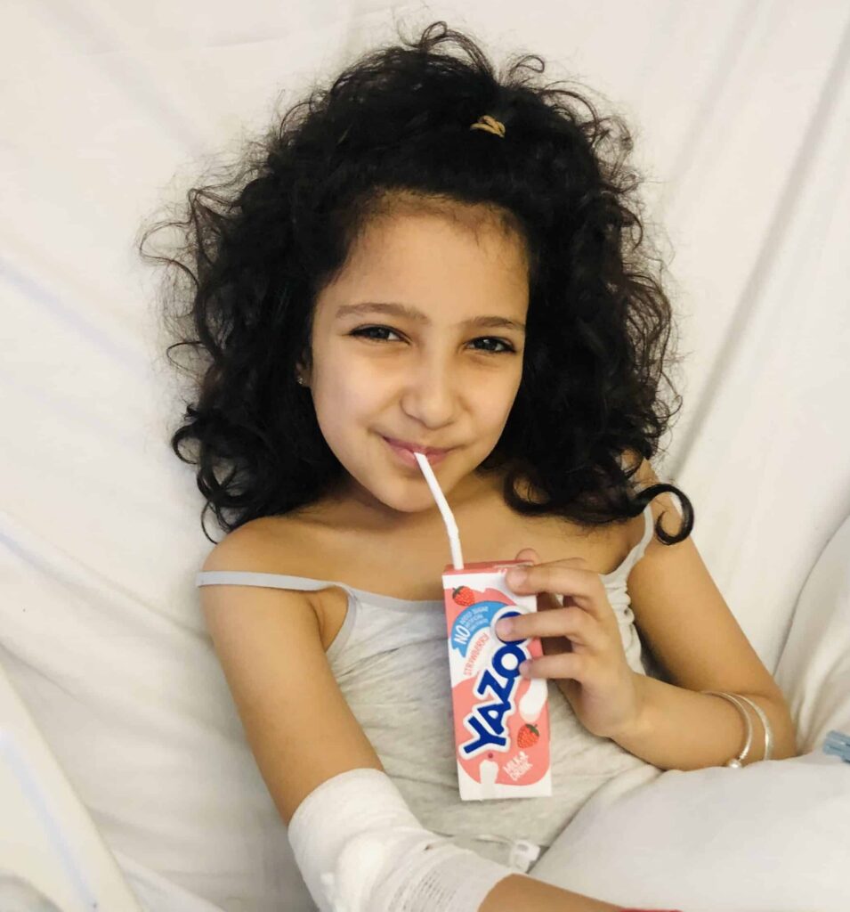 Tia smiling, drinking a carton of strawberry juice, looking at the camera.